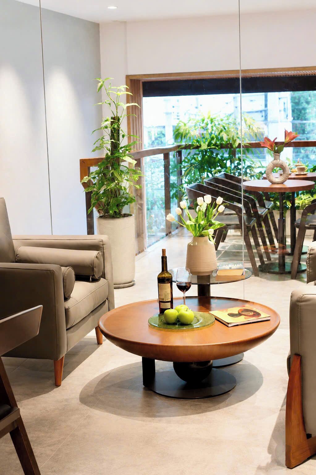 Een moderne woonkamer met een bank, een bijzettafeltje met appels en een fles, en een balkon met planten en een tafel.