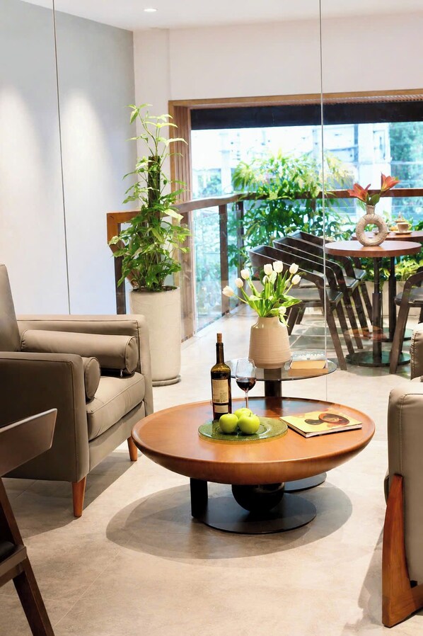 Ein modernes Wohnzimmer mit einer Couch, einem Couchtisch mit Äpfeln und einer Flasche sowie einem Balkon mit Pflanzen und einem Tisch.