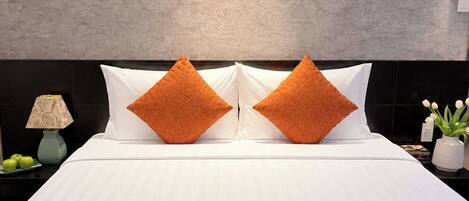 A hotel room with a large bed, two pillows, a nightstand with a lamp, and a wall-mounted light.