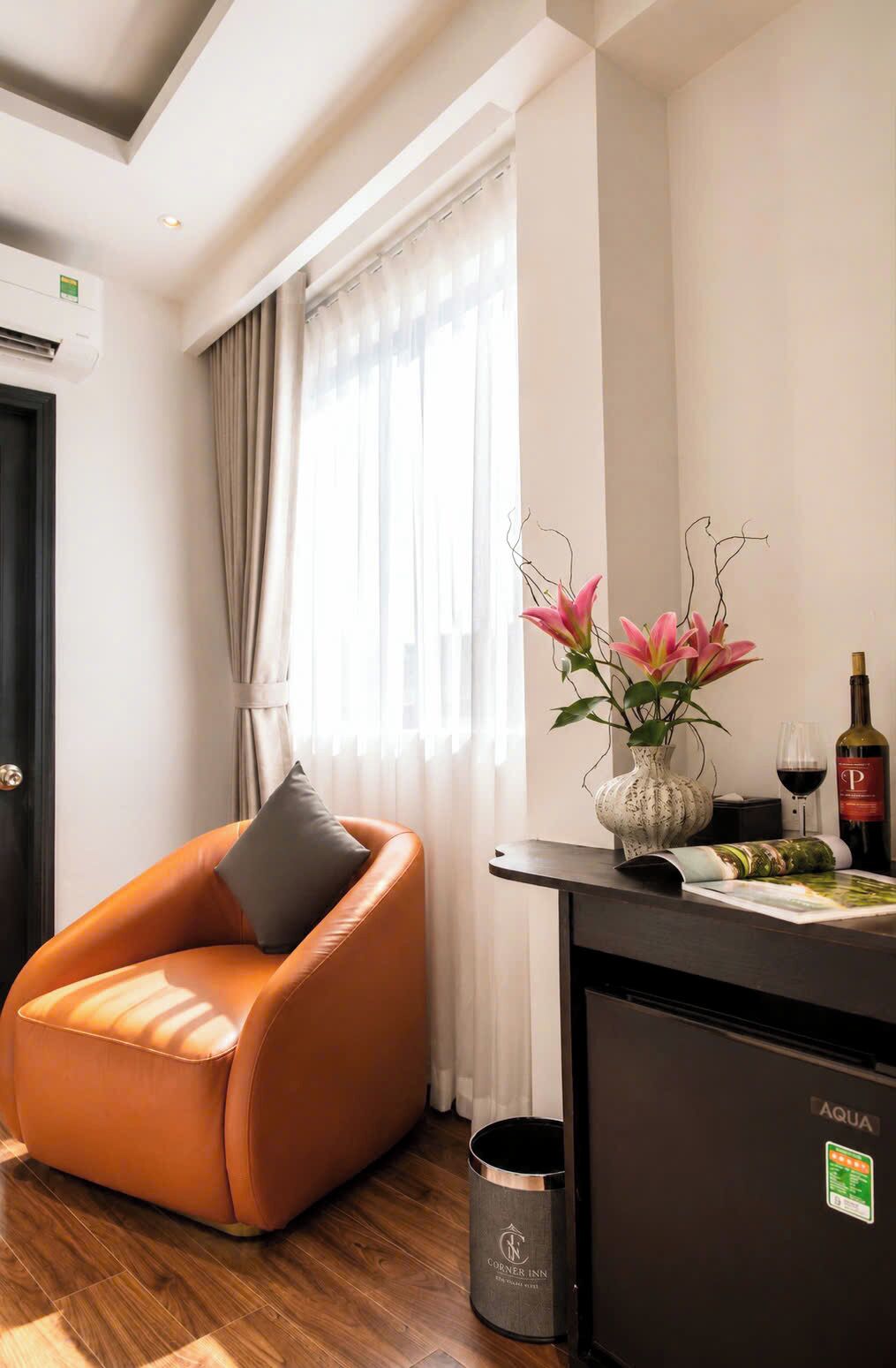 Een moderne hotelkamer met een leren fauteuil, een vaas met bloemen, een wijnfles en een minibar.