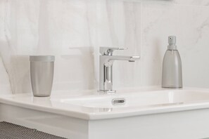 Ein modernes Badezimmer mit einem weißen Waschbecken, einem Chromarmaturen und zwei zylindrischen Behältern auf der Ablagefläche.