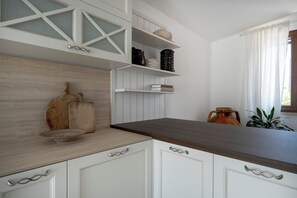 A kitchen with white cabinetry, a wooden countertop, and shelves with various kitchen items. - Beyond the Coni – An Oasis of Relaxation (MONOPOLI)