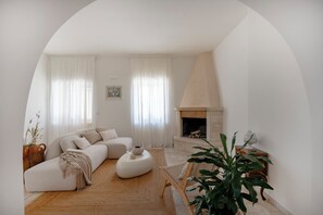 A living room with a sofa, a round coffee table, a fireplace, and a large plant. - Beyond the Coni – An Oasis of Relaxation (MONOPOLI)