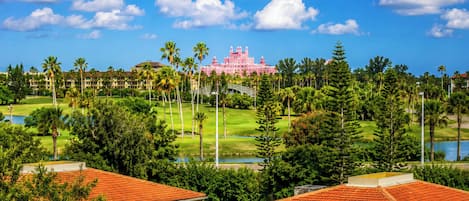 A pink resort with a golf course, palm trees, and a lake.