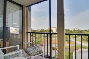 Ein Balkon mit Blick auf eine Wohngegend, ein weißer Stuhl, ein kleiner runder Tisch und ein gestreiftes Kissen.