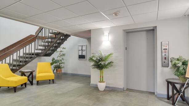 Eine Lobby mit Treppe, zwei gelben Stühlen, einem Blumentopf und einem Aufzug.
