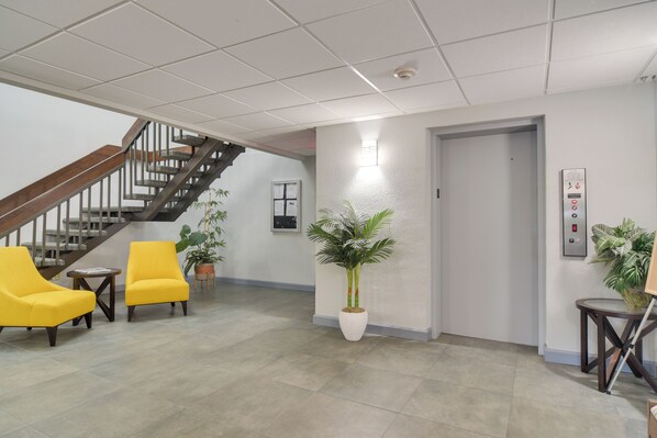 Eine Lobby mit Treppe, zwei gelben Stühlen, einem Blumentopf und einem Aufzug.