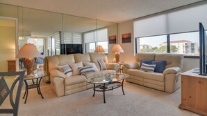 A modern living room with a beige sofa set, a glass coffee table, and a large mirror reflecting the room.