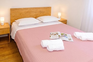 A neatly made bed with a pink bedspread, white pillows, and two bedside lamps. - Twin Apartments With BBQ Area (Okrug)