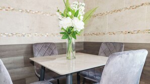 Ein Essbereich mit einem quadratischen Tisch, vier gepolsterten Stühlen und einer Vase mit weißen Blumen.