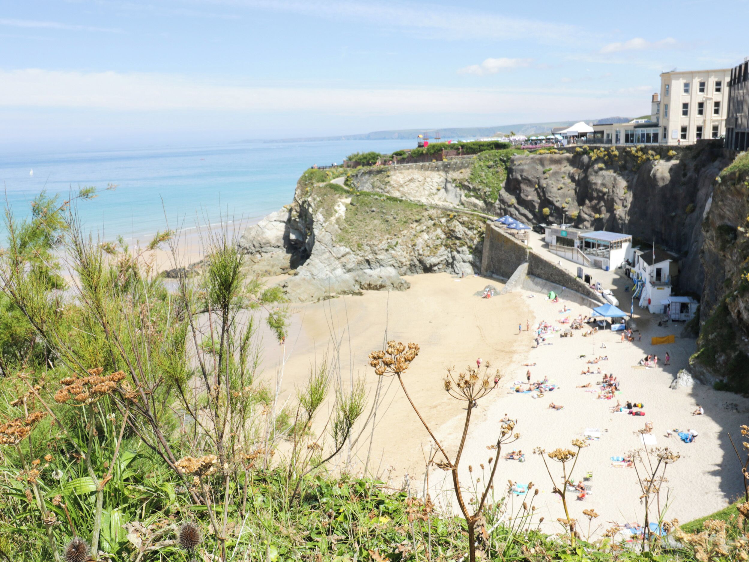 A coastal beach with a rocky cliff, a sandy beach, and a building with a balcony overlooking the sea.
