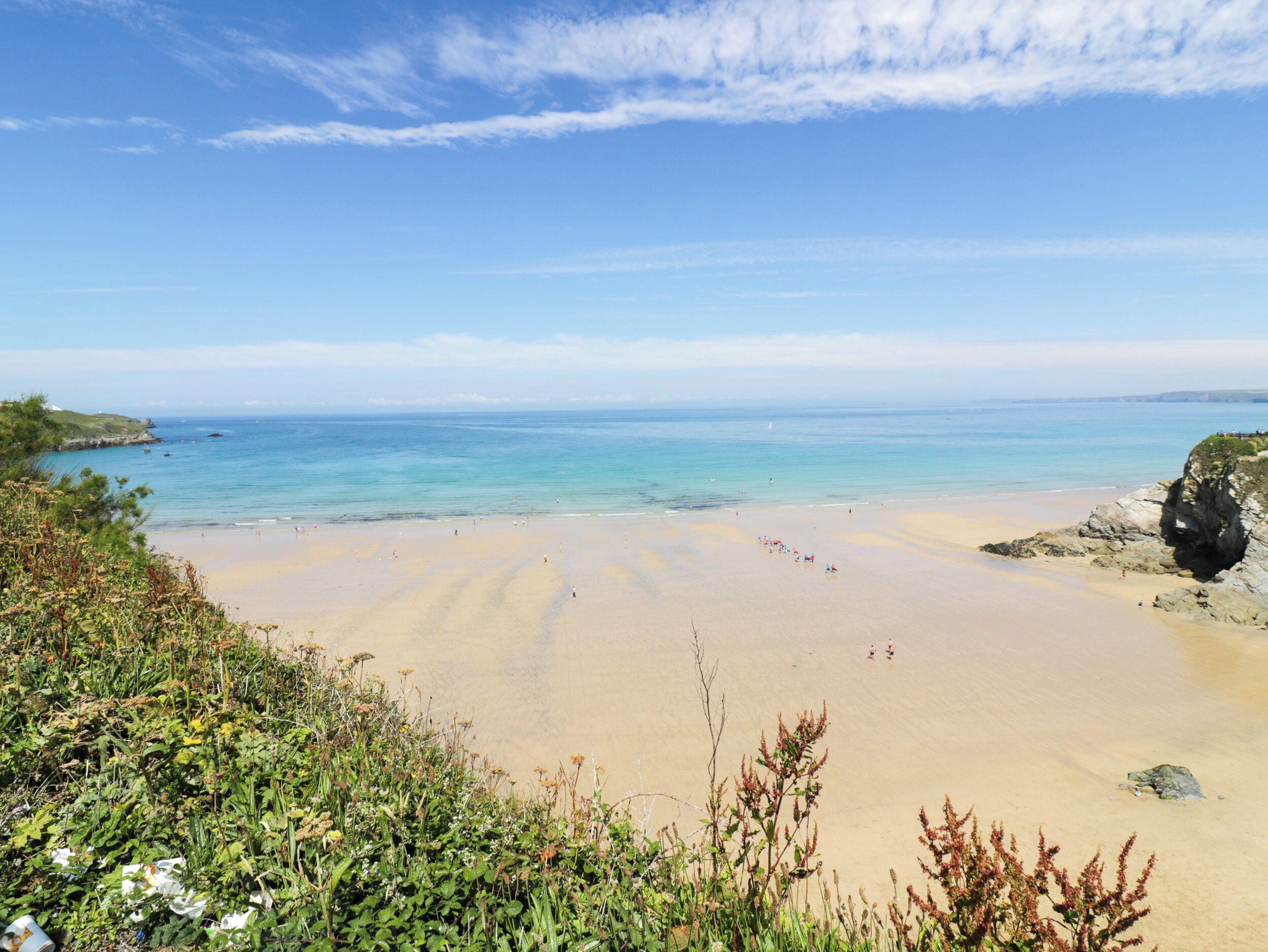 A beach with clear skies, calm waters, and a rocky outcrop on the right.