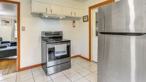 Uma cozinha com geladeira, forno e micro-ondas de aço inoxidável, armários brancos e um extintor de incêndio.