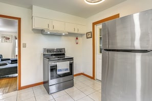 Eine Küche mit Edelstahl-Kühlschrank, Backofen und Mikrowelle, weißen Schränken und einem Feuerlöscher.