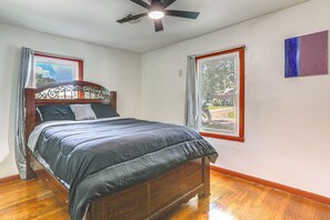 Un dormitorio con cama de madera, ventilador de techo y dos ventanas con cortinas.