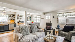 Ein Wohnzimmer mit einer Couch, Sesseln, einem Couchtisch und einer Küche im Hintergrund.