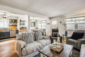 Ein Wohnzimmer mit einer Couch, Sesseln, einem Couchtisch und einer Küche im Hintergrund.
