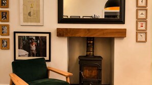 A cozy living room with a green armchair, a fireplace, a large mirror, and framed artwork on the wall. - Ivy & Ink Cottage - Inverness (Inverness)
