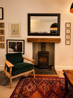 A cozy living room with a green armchair, a fireplace, a large mirror, and framed artwork on the wall. - Ivy & Ink Cottage - Inverness (Inverness)