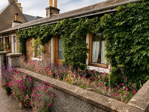 A traditional stone building with ivy-covered walls, a stone pathway, and vibrant flowers. - Ivy & Ink Cottage - Inverness (Inverness)