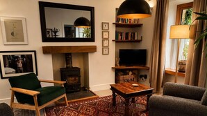 A cozy living room with a fireplace, a television, and a bookshelf. - Ivy & Ink Cottage - Inverness (Inverness)