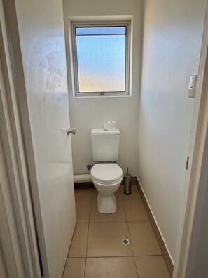 A small, narrow bathroom with a toilet, a window, and a trash bin. - A beautiful room in Clayfield, Brisbane - 10 min to the airport! (Clayfield)