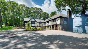 A large, two-story house with a stone chimney, surrounded by a well-maintained lawn and trees. - Luxury Tudor Estate | Pool, Spa and Valley Views (Hazleton)