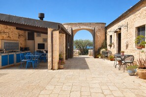 An outdoor patio area with stone flooring, blue metal chairs, a stone archway, and potted plants. - La Muraglia by Geco Vacation Rentals (Santa Croce Camerina)