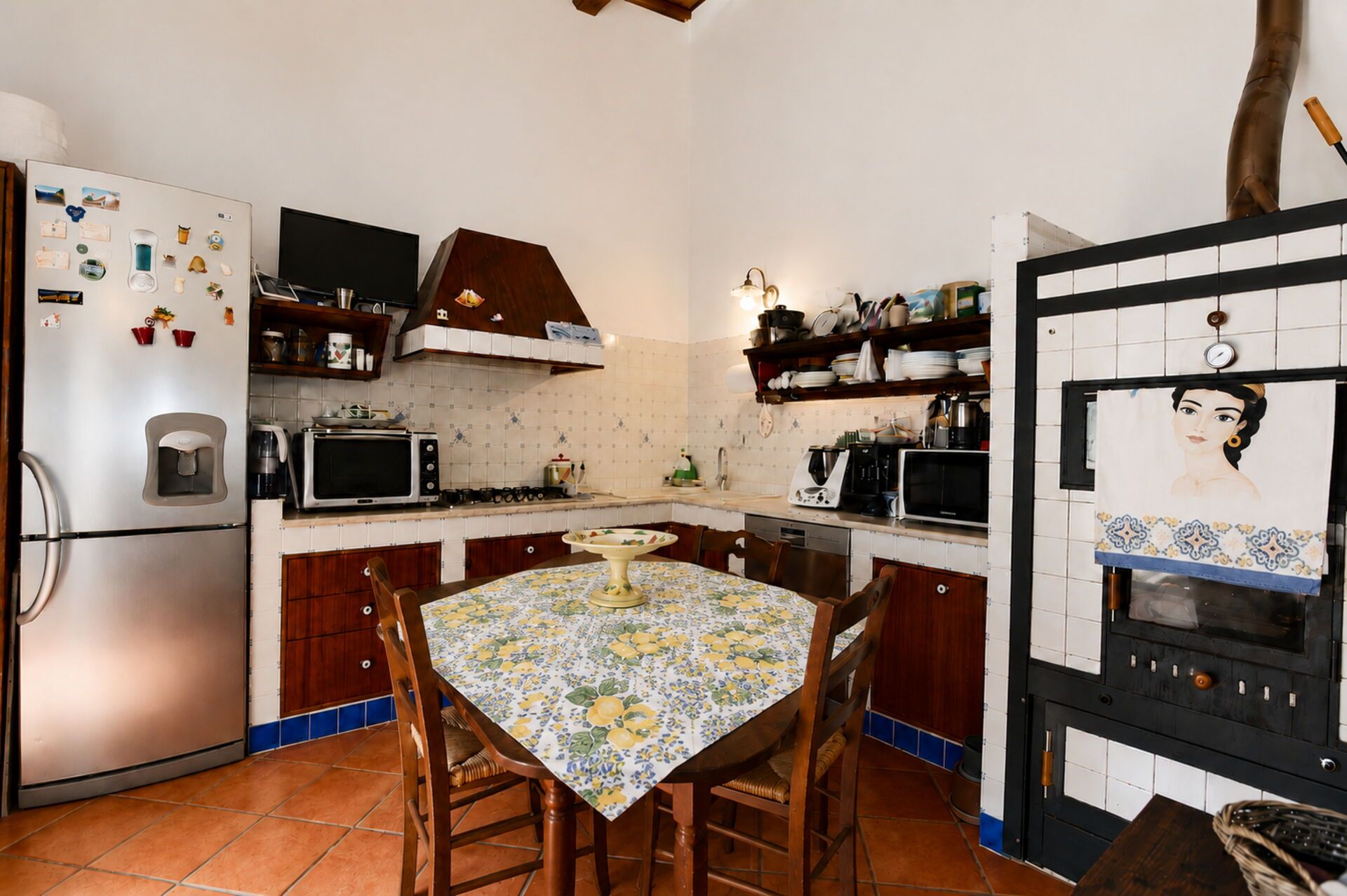 A compact kitchen with a refrigerator, microwave, stove, and oven. There is a dining table with chairs and a wall-mounted oven.