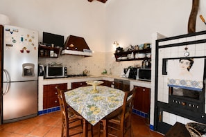 A compact kitchen with a refrigerator, microwave, stove, and oven. There is a dining table with chairs and a wall-mounted oven. - La Muraglia by Geco Vacation Rentals (Santa Croce Camerina)