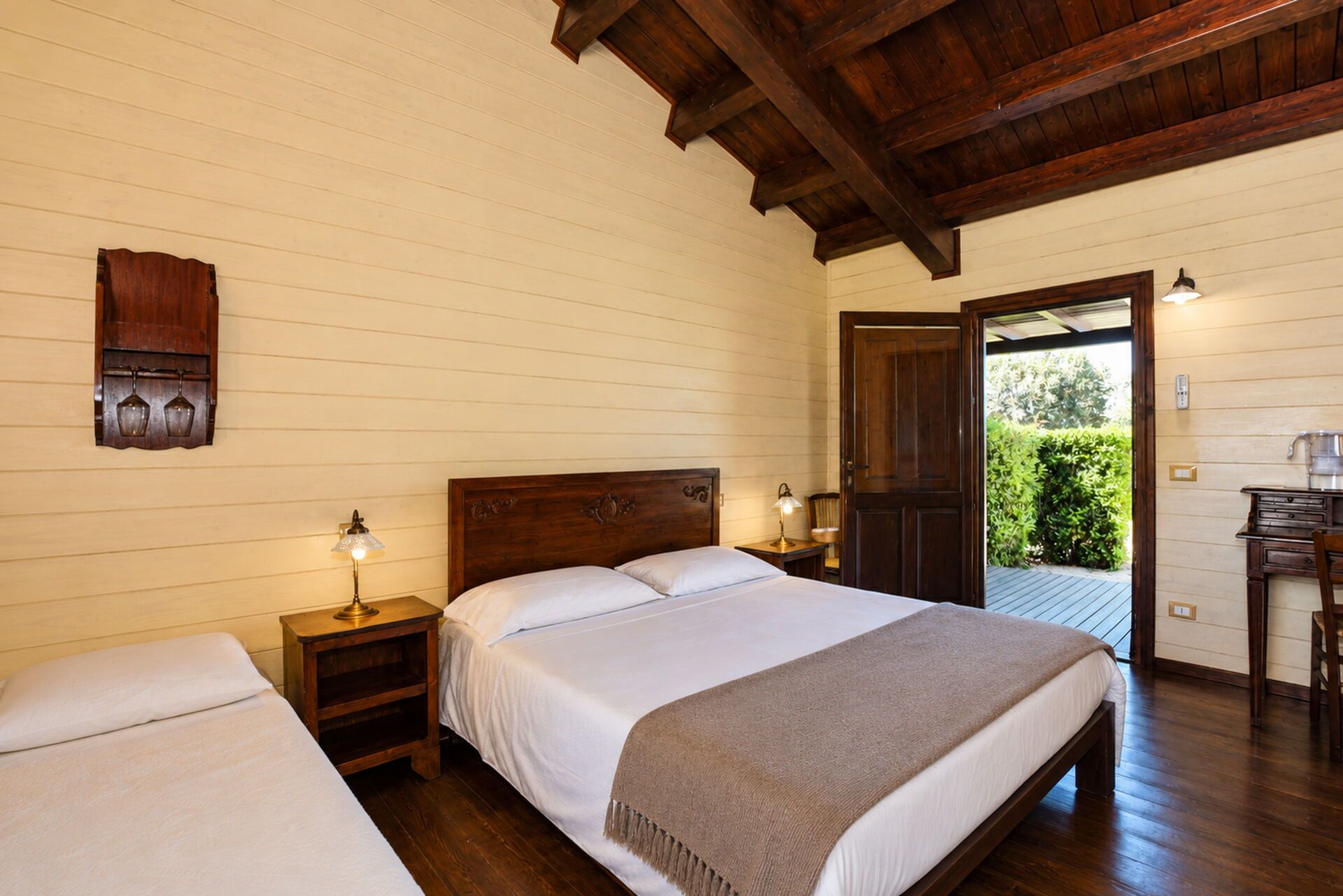 Une chambre d’hôtel avec un plafond en bois, un lit avec une literie blanche, une table de chevet avec une lampe, et une vue sur la verdure à l’extérieur.