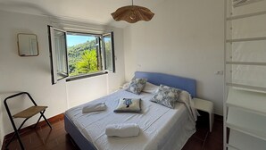 A bedroom with a bed, a chair, a window with a view, and a hanging light fixture. - Il Fienile, Garden and Peacefull View (Arnasco)