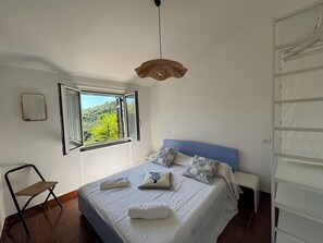 Ein Schlafzimmer mit Bett, Stuhl, Fenster und Pendelleuchte.
