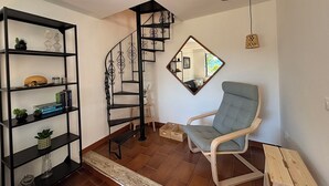 A room with a spiral staircase, a mirrored wall, a wooden chair, and a black shelving unit with decorative items. - Il Fienile, Garden and Peacefull View (Arnasco)