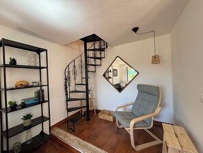 Ein Zimmer mit einer Wendeltreppe, einer Spiegelwand, einem Holzstuhl und einer schwarzen Regaleinheit mit Dekorationselementen.
