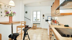 A kitchen with wooden cabinets, a stove, and a dining area with a chair and stools. - Newly renovated three-story 16th-century house in central Ceret (Céret)