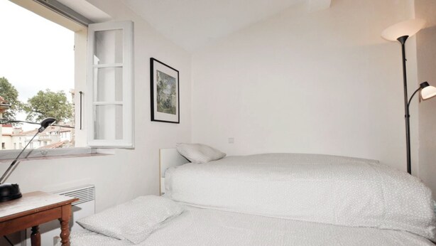 A bedroom with a bed, a bedside table, a lamp, a window, and a framed picture on the wall. - Newly renovated three-story 16th-century house in central Ceret (Céret)