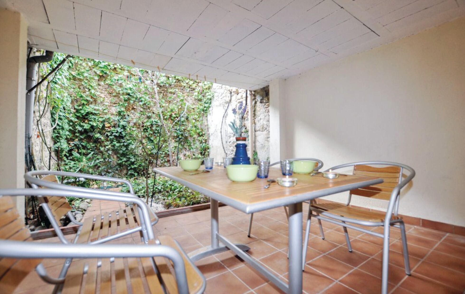 Um pátio externo com mesa e cadeiras, com vista para um jardim.