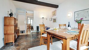 A dining area with a wooden table, chairs, and a white rug. There is a wooden cabinet to the left and a doorway leading to another room. - Newly renovated three-story 16th-century house in central Ceret (Céret)