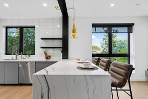 Cocina moderna con una isla de mármol, electrodomésticos de acero inoxidable y grandes ventanales con vistas a zonas verdes.