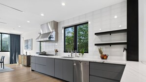 A modern kitchen with a large island, stainless steel appliances, and a view of greenery outside. - Rooftop + Grill | Venice Canals + Abbot Kinney | Canal Crown (Los Angeles)