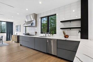 A modern kitchen with a large island, stainless steel appliances, and a view of greenery outside. - Rooftop + Grill | Venice Canals + Abbot Kinney | Canal Crown (Los Angeles)