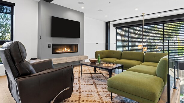 A modern living room with a fireplace, a flat-screen TV, a green sofa, and a leather chair. - Rooftop + Grill | Venice Canals + Abbot Kinney | Canal Crown (Los Angeles)