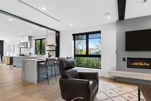 Una sala de estar moderna con chimenea, un ventanal grande y una cocina al fondo.