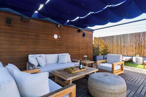 An outdoor seating area with a wooden deck, a covered section with blue fabric, and a wooden wall with a clock. - Rooftop + Grill | Venice Canals + Abbot Kinney | Canal Crown (Los Angeles)