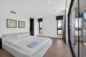 A modern bedroom with a large bed, two framed artworks, a window with curtains, and a door leading to another room. - Rooftop + Grill | Venice Canals + Abbot Kinney | Canal Crown (Los Angeles)