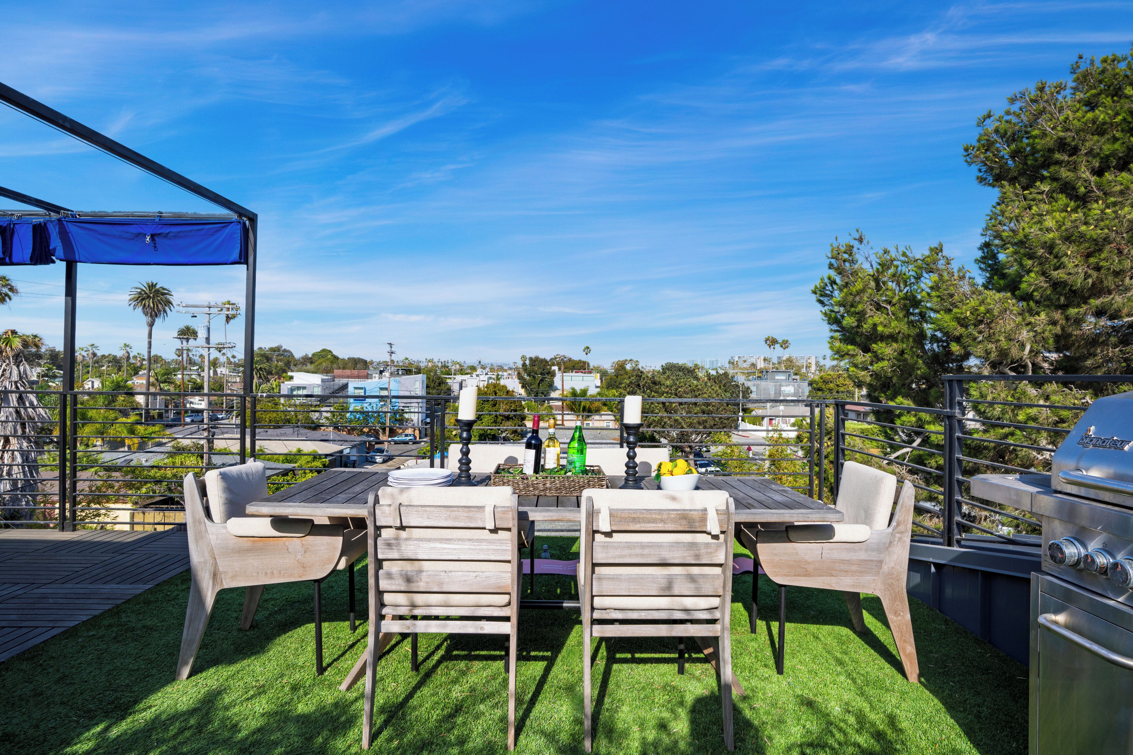 An outdoor patio with a table and chairs, a grill, and a view of the cityscape.