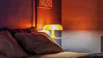 Um quarto com cama, almofadas, mesa de cabeceira com abajur e decoração de parede estampada.