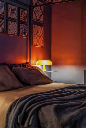 A bedroom with a bed, pillows, a bedside table with a lamp, and patterned wall decor. - Le stanze al genio di Darlon (Palermo)