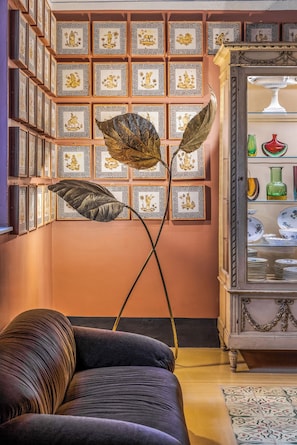 A room with a sofa, a decorative floor lamp, a wall with framed artwork, and a cabinet with dishes. - Le stanze al genio di Darlon (Palermo)
